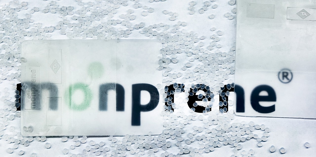 Clear Monprene TPE plaque surrounded by translucent polymer pellets with Monprene branding visible